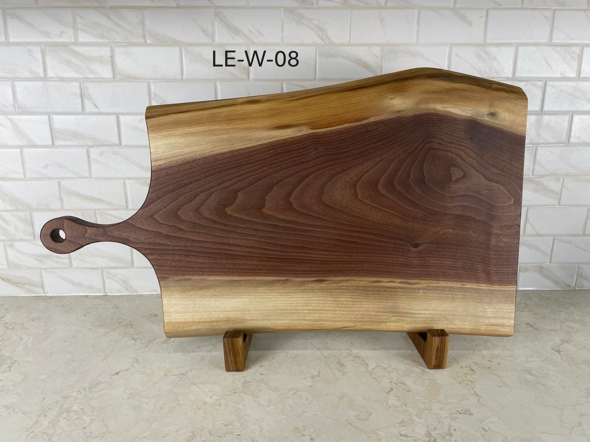 Wooden cutting board with a handle on a light gray surface and white tiled wall background.